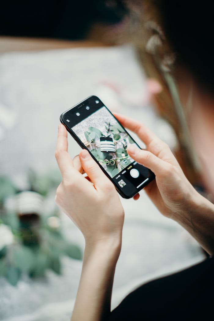 Photo of a person using a smartphone to capture a bouquet of flowers, indoors with natural lighting.